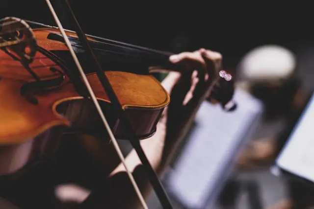 Close-up of a musician playing a violin, with sheet music blurred in the background.
